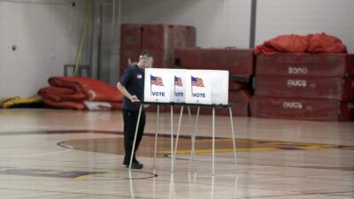 Doug Milks disinfects voting booths after being used as voters, ignoring a stay-at-home order over the coronavirus threat, cast ballots in the state's presidential primary election in the gym at East High School, Tuesday, April 7, 2020 in Madison, Wis. (Steve Apps/Wisconsin State Journal via AP)