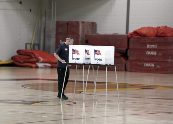 Doug Milks disinfects voting booths after being used as voters, ignoring a stay-at-home order over the coronavirus threat, cast ballots in the state's presidential primary election in the gym at East High School, Tuesday, April 7, 2020 in Madison, Wis. (Steve Apps/Wisconsin State Journal via AP)