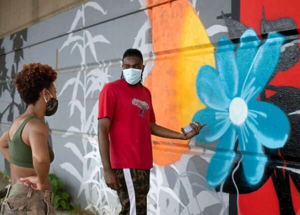Camerin “Camo” Nesbit gives tips on working with aerosol to fellow muralist Janel Young as they add to a Black Lives Matter mural along the Allegheny River in downtown Pittsburgh. The mural was created by a group of white house painters. (photograph by Martha Rial)