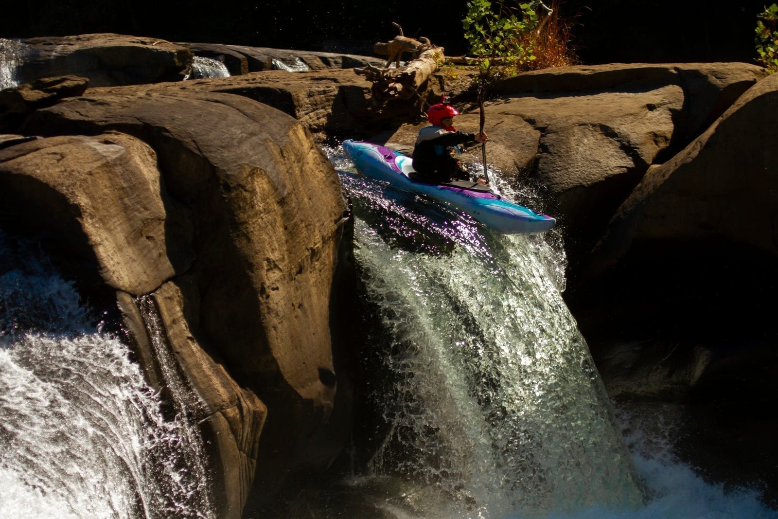 A kayaker wearing a red helmet with camera attached descends down a fast-flowing, rocky waterfall in Ohiopyle Falls, located in the Laurel Highlands in Western Pennsylvania.
