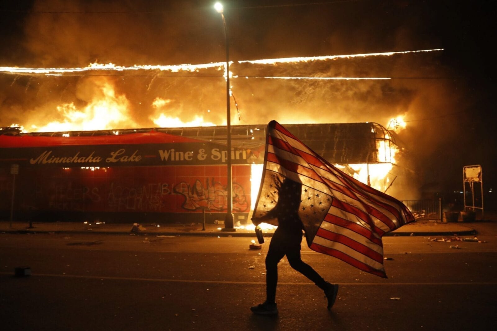 A protester carries a U.S. flag upside down, a sign of distress, next to a burning building Thursday, May 28, 2020, in Minneapolis. Protests over the death of George Floyd, a Black man who died in police custody on May 25, broke out in Minneapolis for a third straight night. (AP Photo/Julio Cortez)