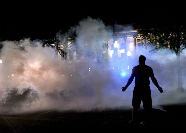 A protester attempts to continue standing through a cloud of tear gas fired by police outside the Kenosha County Courthouse, late Monday, Aug. 24, 2020, in Kenosha, Wis. Protesters converged on the county courthouse during a second night of clashes after the police shooting of Jacob Blake a day earlier turned Kenosha into the nation's latest flashpoint city in a summer of racial unrest. (AP Photo/David Goldman)