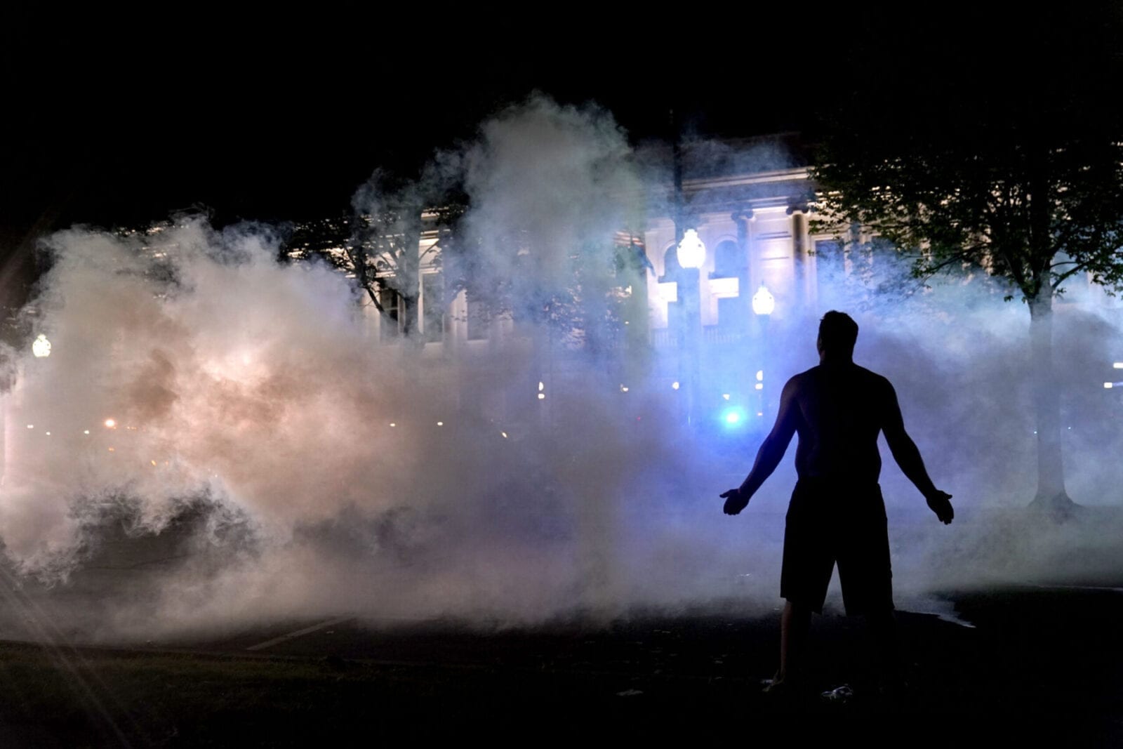 A protester attempts to continue standing through a cloud of tear gas fired by police outside the Kenosha County Courthouse, late Monday, Aug. 24, 2020, in Kenosha, Wis. Protesters converged on the county courthouse during a second night of clashes after the police shooting of Jacob Blake a day earlier turned Kenosha into the nation's latest flashpoint city in a summer of racial unrest. (AP Photo/David Goldman)