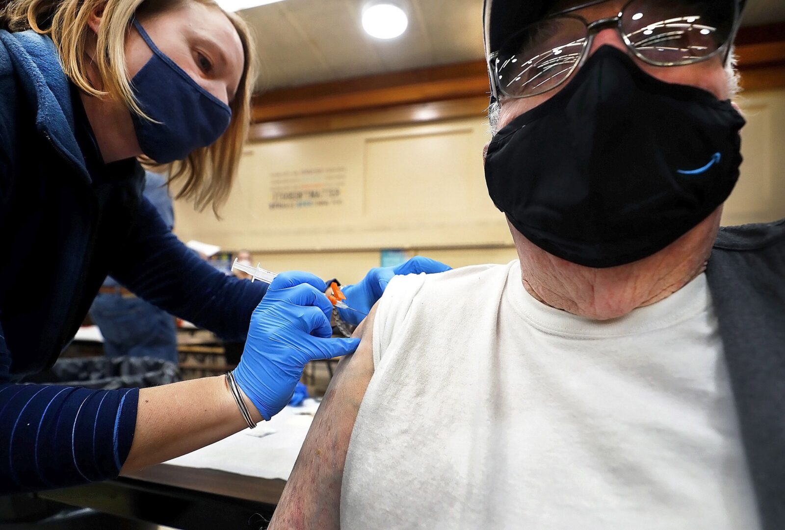 Amber Pedro, a volunteer from Family Practice Laporte, administers the vaccine into the arm of Robert Keen, 84 of Forksville, in the cafeteria of the Sullivan County Elementary School. (Fred Adams / Spotlight PA)