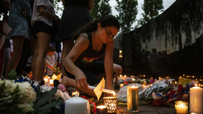 Dozens of mourners gather for a vigil near Central Avenue and St Johns Avenue in downtown Highland Park, one day after a gunman killed at least seven people and wounded dozens more by firing an AR-15-style rifle from a rooftop onto a crowd attending Highland Park's Fourth of July parade, Tuesday, July 5, 2022 in Highland Park, Ill.. (Ashlee Rezin/Chicago Sun-Times via AP)