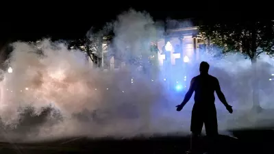 A protester attempts to continue standing through a cloud of tear gas fired by police outside the Kenosha County Courthouse, late Monday, Aug. 24, 2020, in Kenosha, Wis. Protesters converged on the county courthouse during a second night of clashes after the police shooting of Jacob Blake a day earlier turned Kenosha into the nation's latest flashpoint city in a summer of racial unrest. (AP Photo/David Goldman)